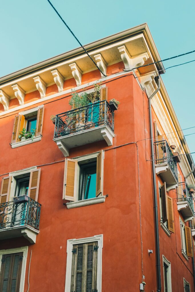 pexels-photo-5227434-5227434 Italian architecture showcasing a rustic red exterior with ornate balconies and shutters.